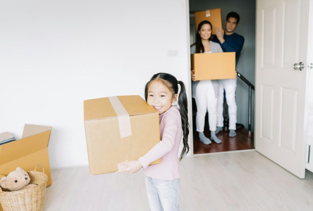 Portrait of a happy asian little daughter carrying boxes into the a new home on moving day.